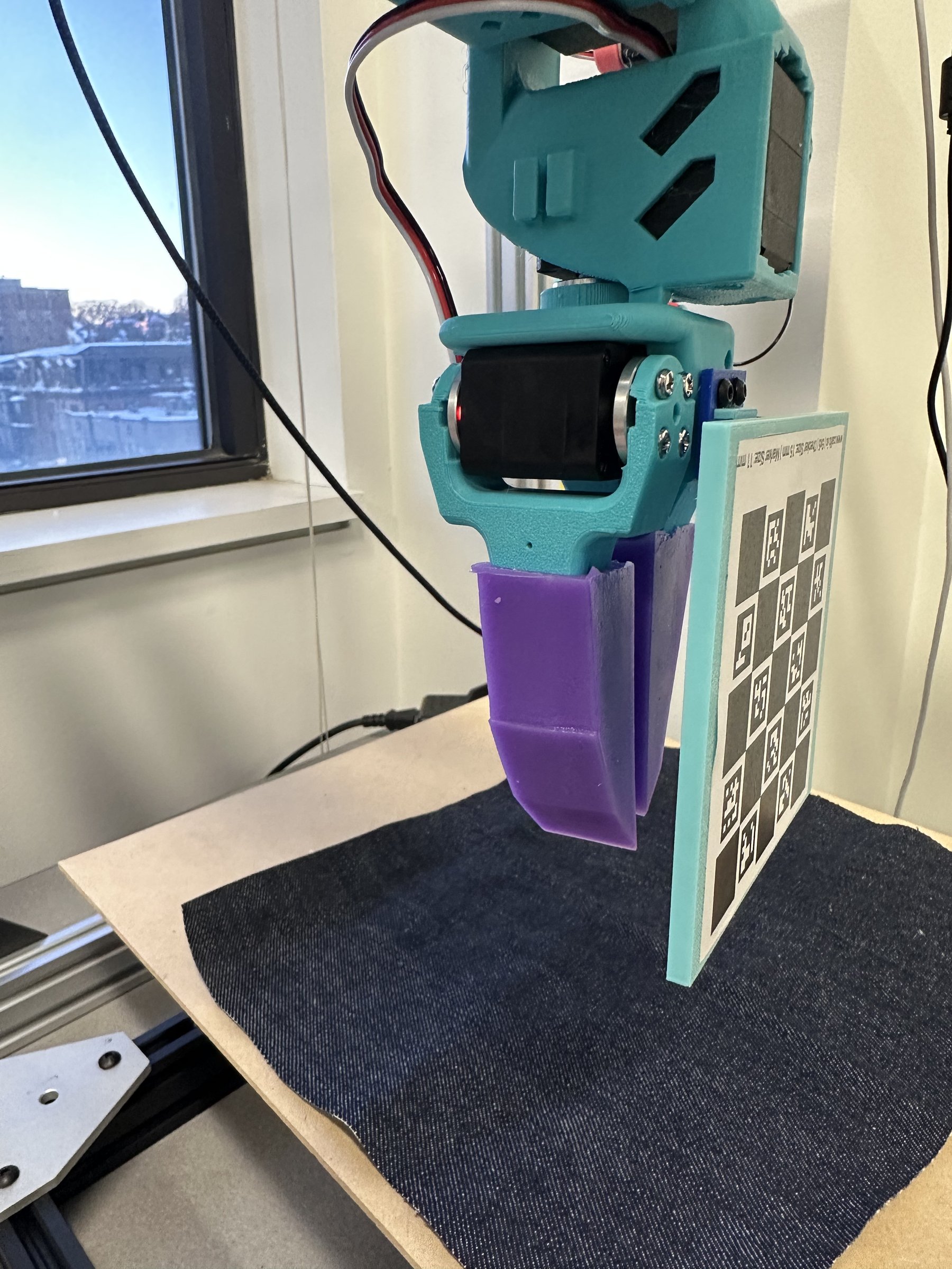Physical gripper with purple silicone tip and ChAruco calibration board on denim fabric