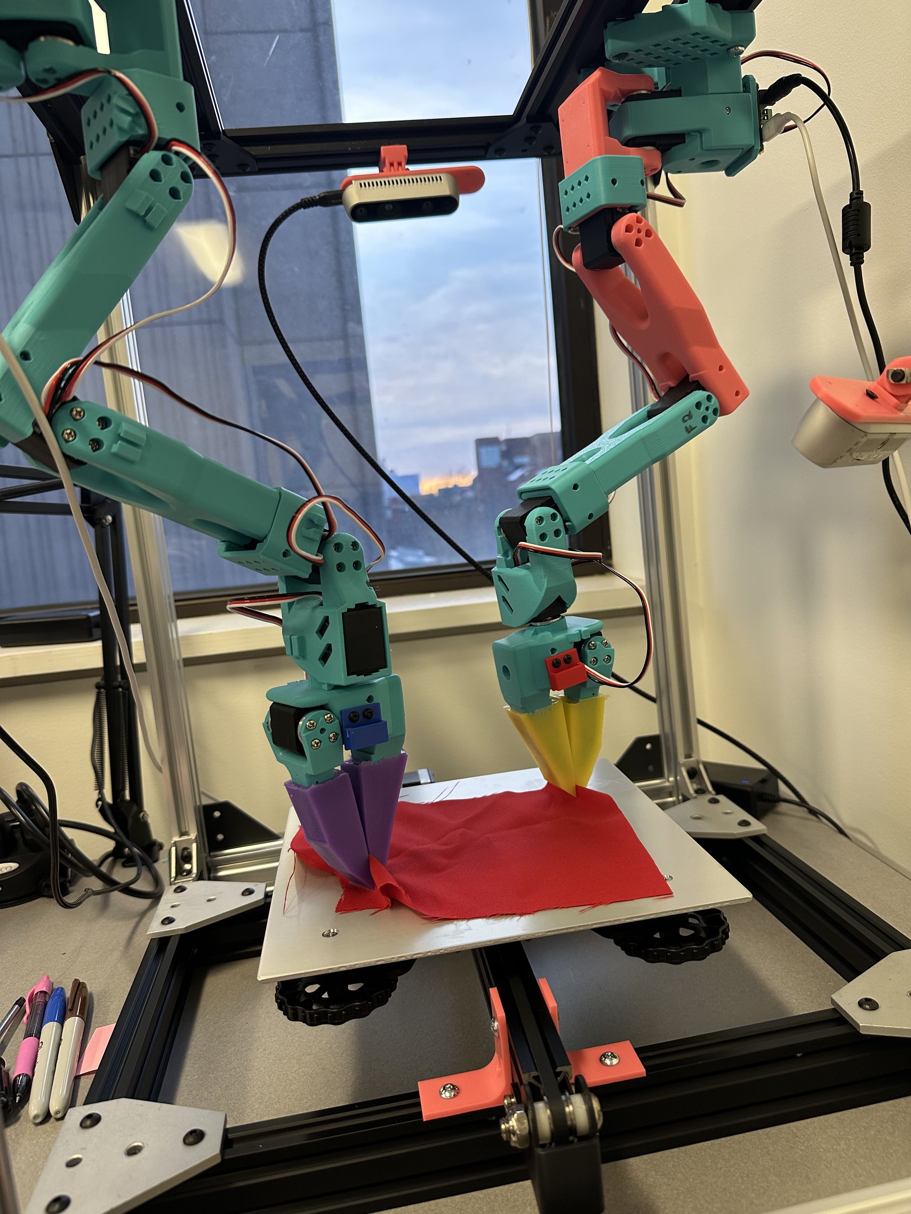 Both follower arms pinching red cloth with silicone gripper tips