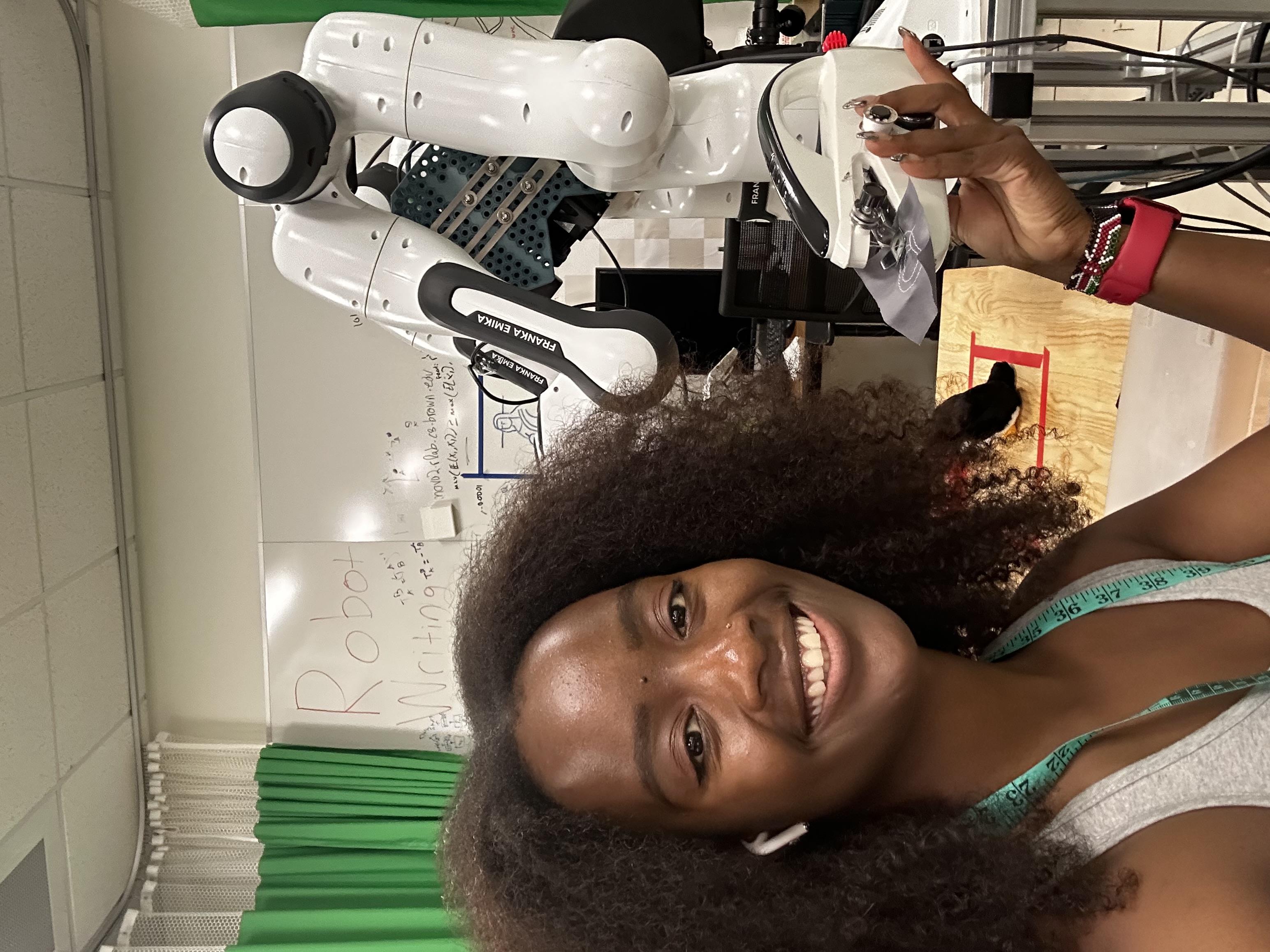 Tabby holding a handheld sewing machine against a Franka robot arm
