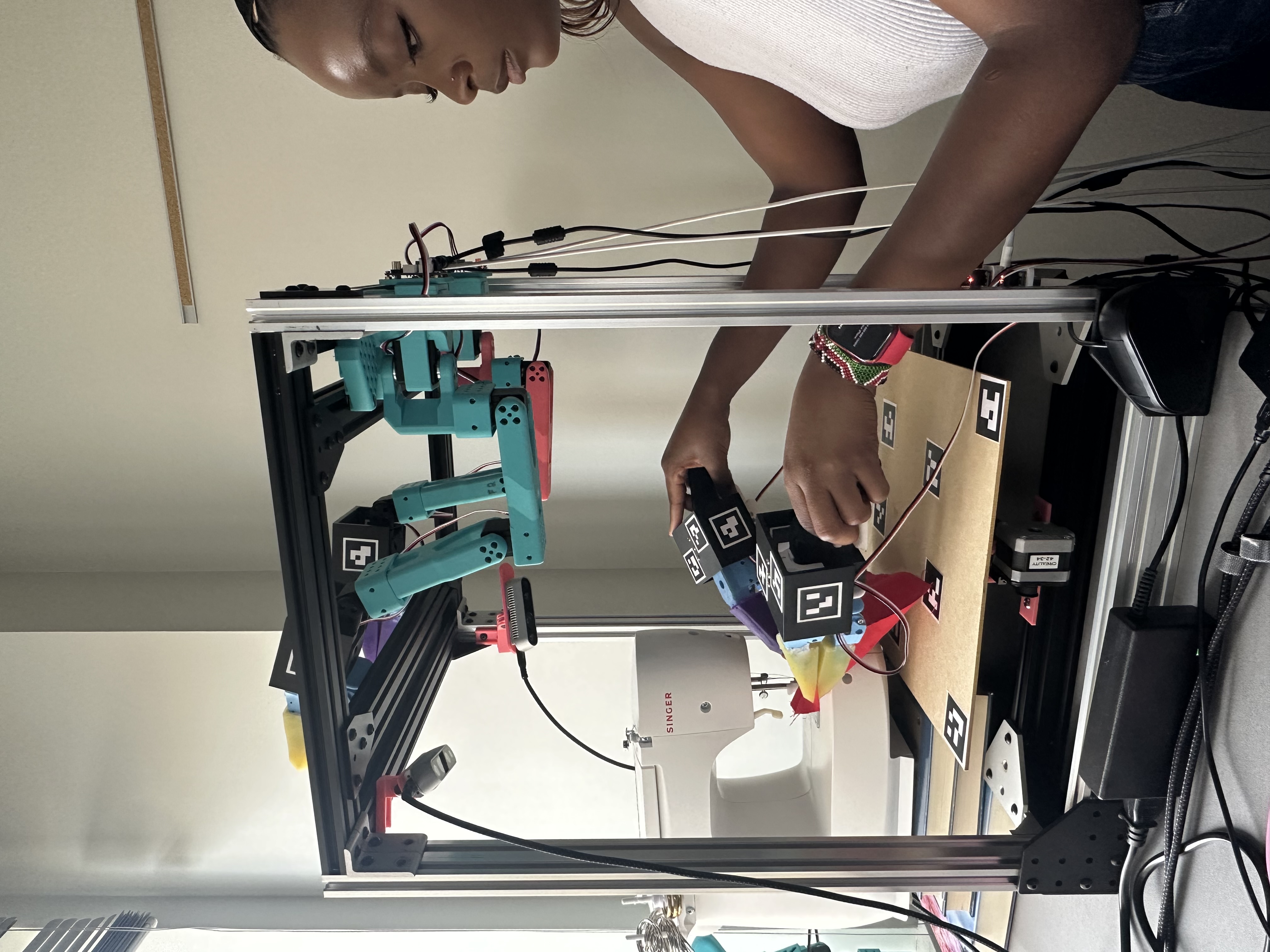 Tabby using handheld grippers to manipulate cloth on the sewing machine inside the robot cell